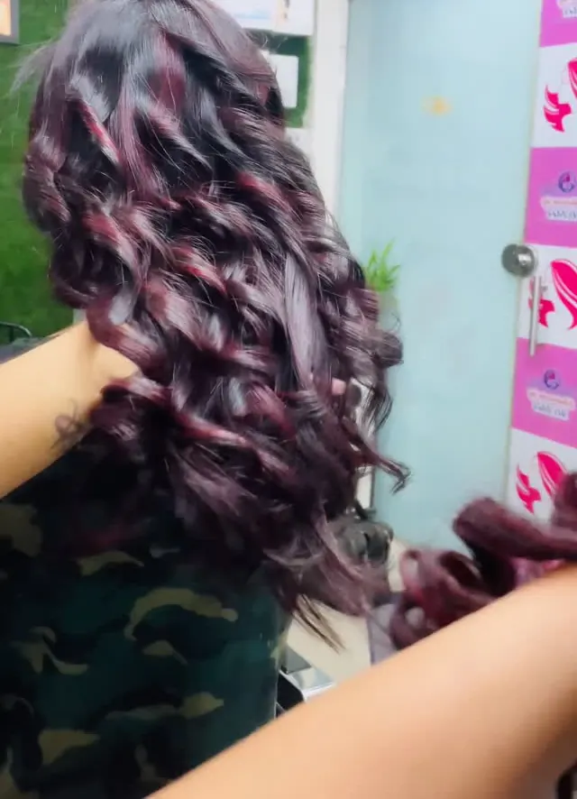 Long hair in soft burgundy and brown balayage, coloured without bleach, styled in loose curls.