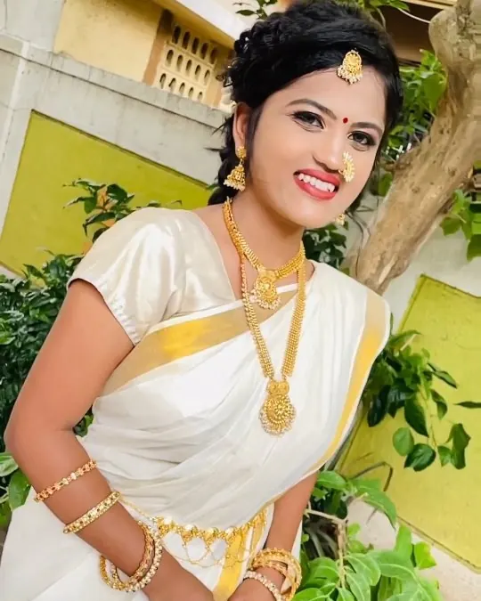 South Indian bride in a white and gold kasavu saree with temple jewellery, smiling.